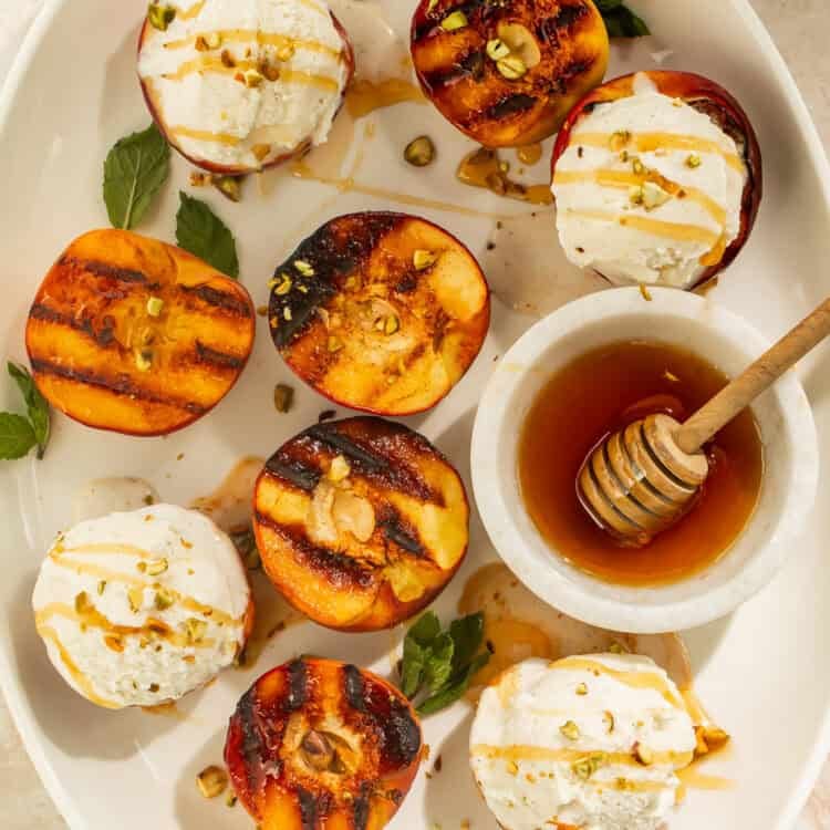 Grilled peaches topped with vanilla ice cream, honey, and pistachios on a serving platter