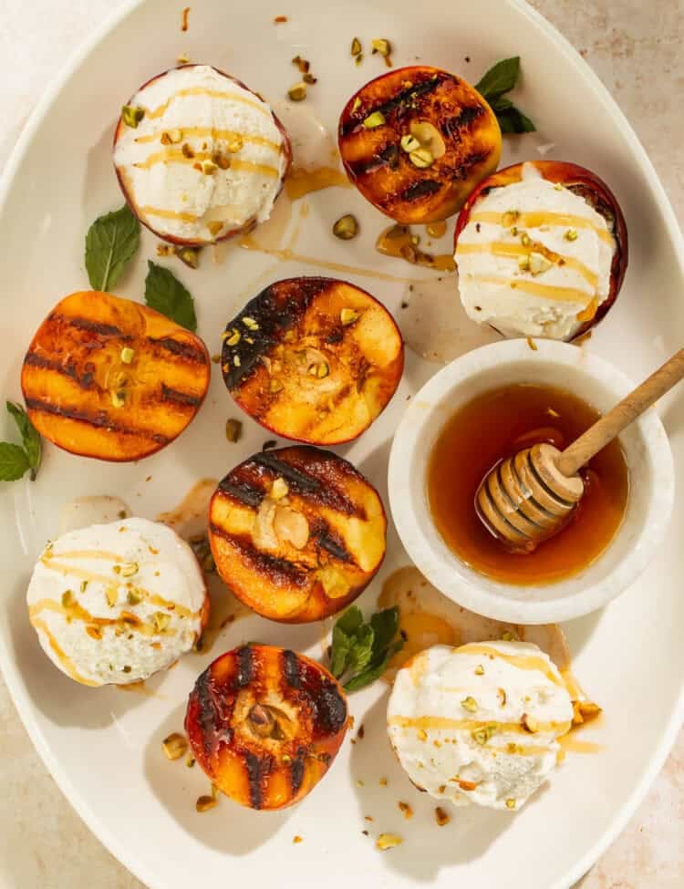 Grilled peaches topped with vanilla ice cream, honey, and pistachios on a serving platter