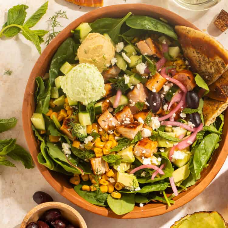 Overhead view of a harissa avocado bowl with pita, olives, and harissa vinaigrette