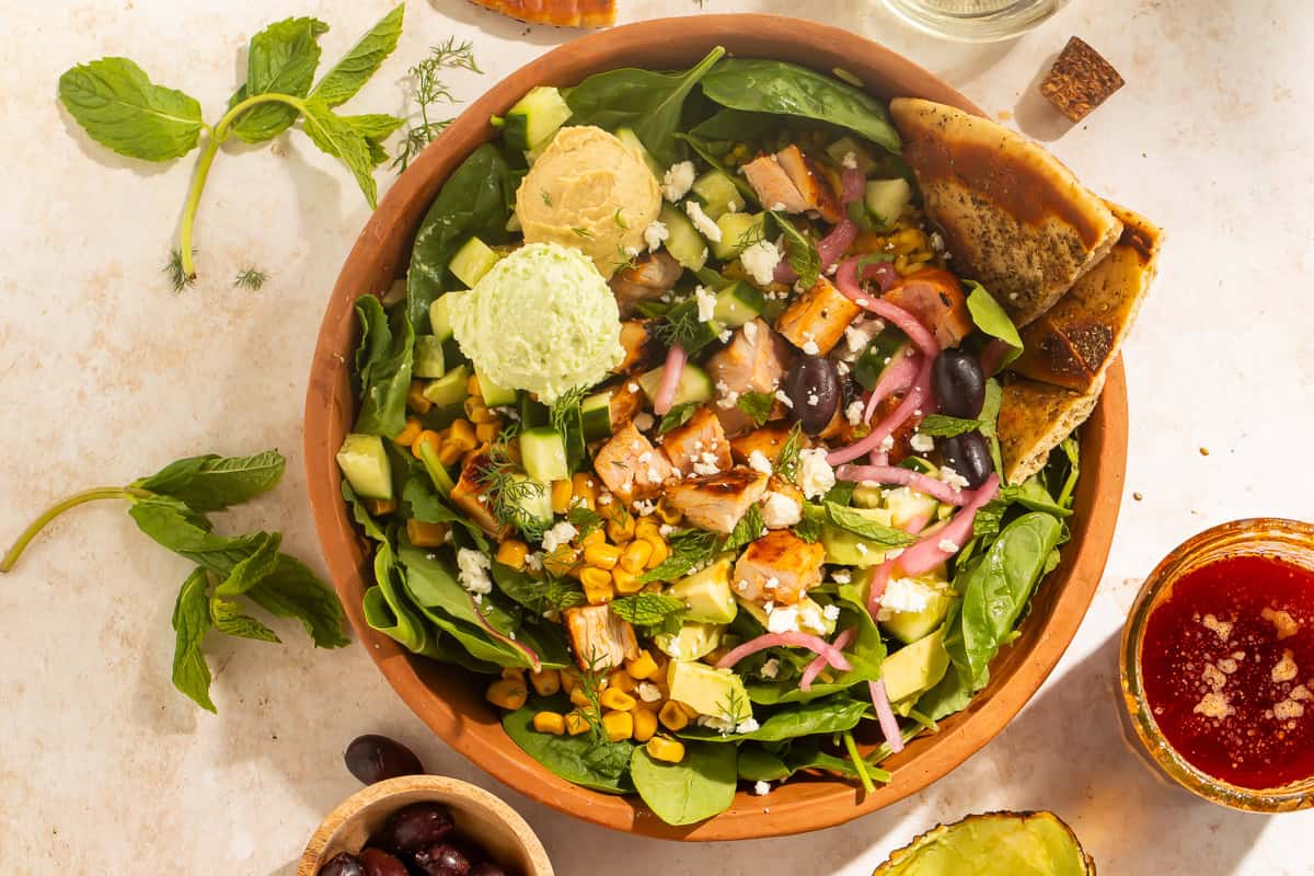 Overhead view of a harissa avocado bowl with pita, olives, and harissa vinaigrette