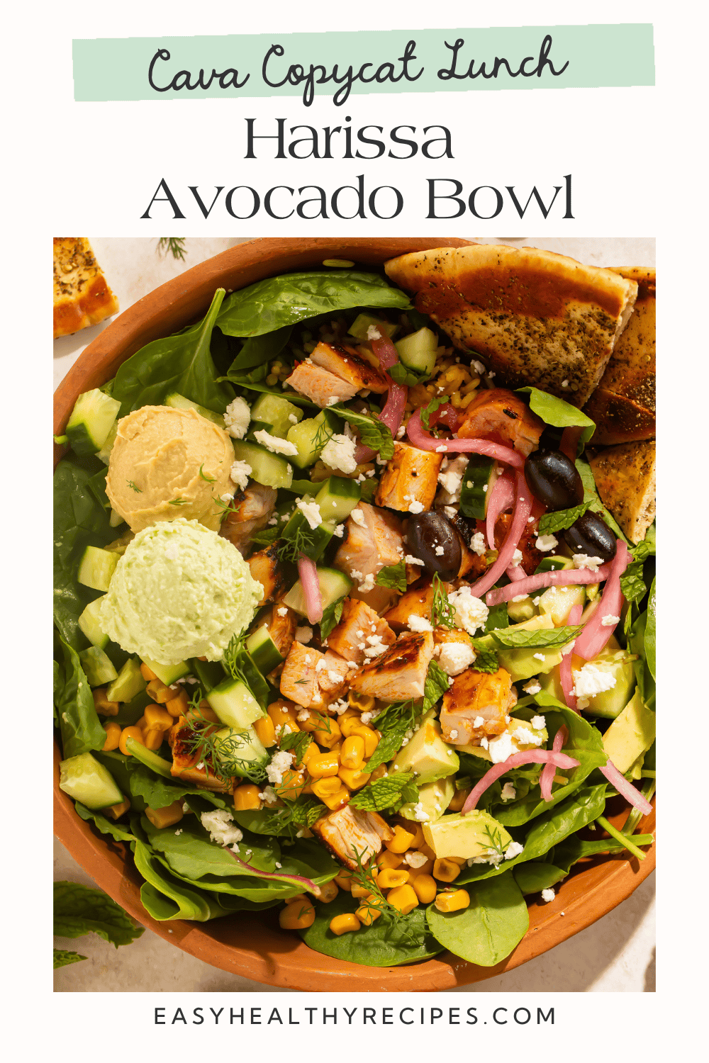 Harissa avocado bowl with sliced chicken, crazy feta, hummus, avocado, and pickled red onions in a terracotta bowl