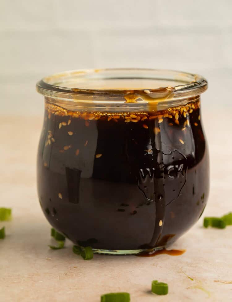 Homemade teriyaki sauce in a glass jar with sesame seeds and green onions.