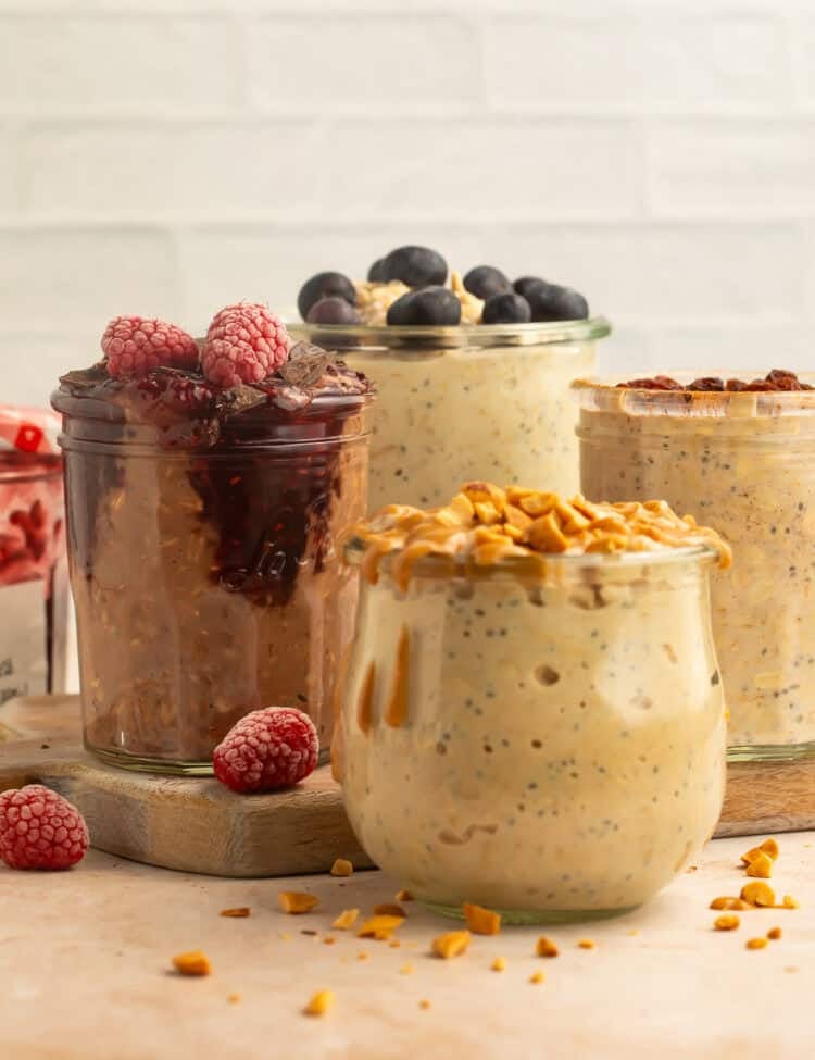 Mixed vegan overnight oats flavors in glass jars with fruit, nuts, and jam toppings