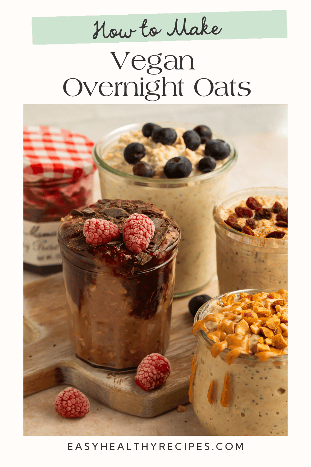 Four glass jars of vegan overnight oats with blueberry, chocolate raspberry, raisin, and peanut butter toppings on a wooden surface