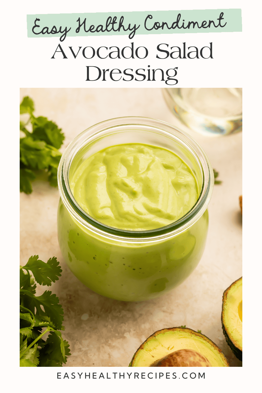 Smooth avocado salad dressing in a small glass jar garnished with fresh cilantro and avocado on a light countertop