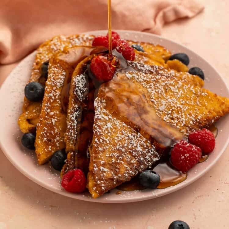 Maple syrup poured over keto French toast topped with fresh raspberries, blueberries, and powdered sweetener.