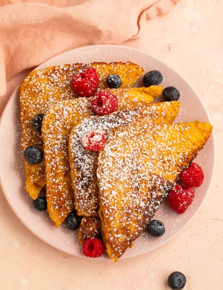 Keto French toast dusted with powdered sweetener and topped with fresh raspberries and blueberries on a pink plate.