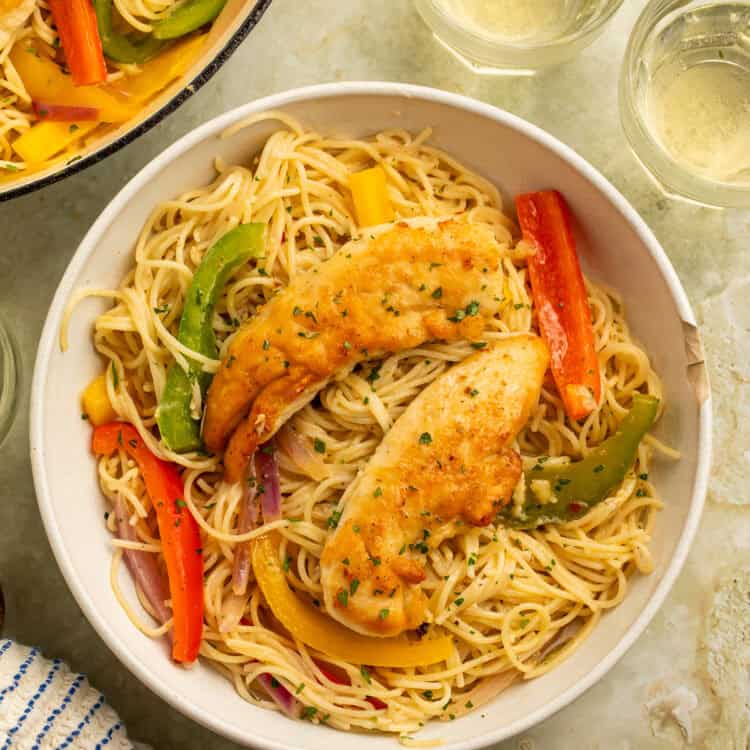 Bowl of Olive Garden chicken scampi with golden chicken tenders, angel hair pasta, colorful peppers, and red onion.