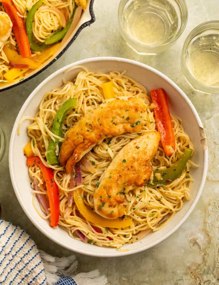 Bowl of Olive Garden chicken scampi with golden chicken tenders, angel hair pasta, colorful peppers, and red onion.