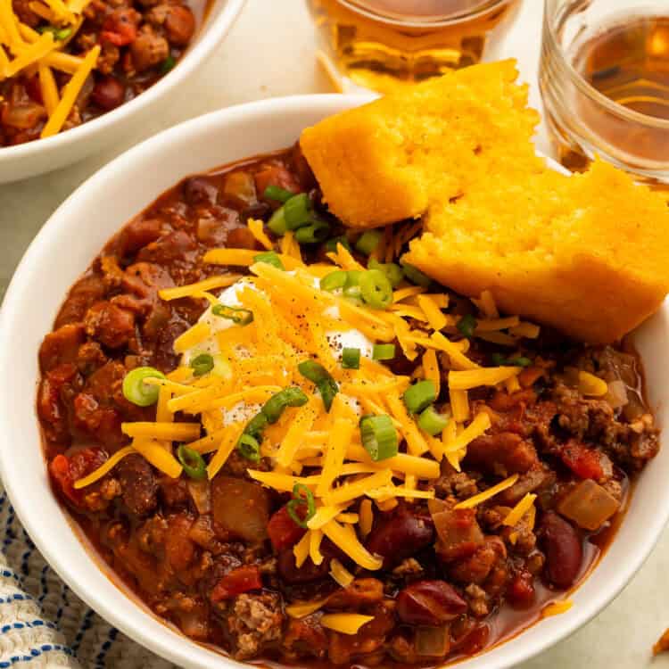 Bowl of ground bison chili topped with cheddar, sour cream, and green onions and served with cornbread.