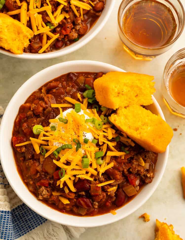 Overhead view of two bowls of bison chili with cheese, sour cream, green onions, and cornbread.