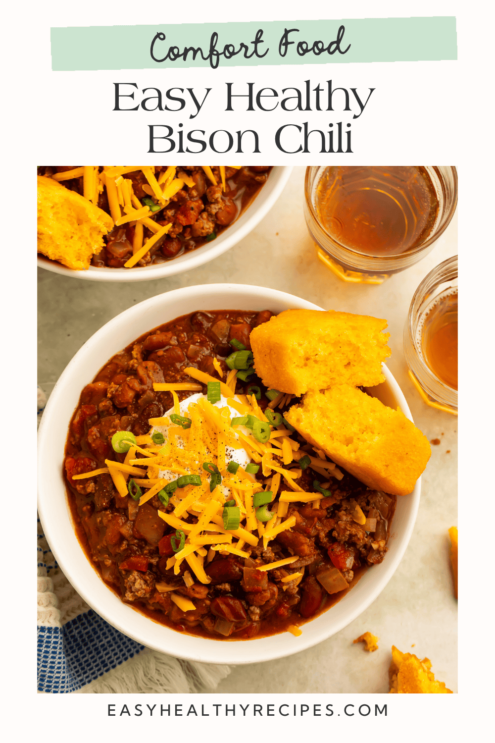 Comfort food graphic showing two bowls of bison chili topped with cheddar, sour cream, and green onions.