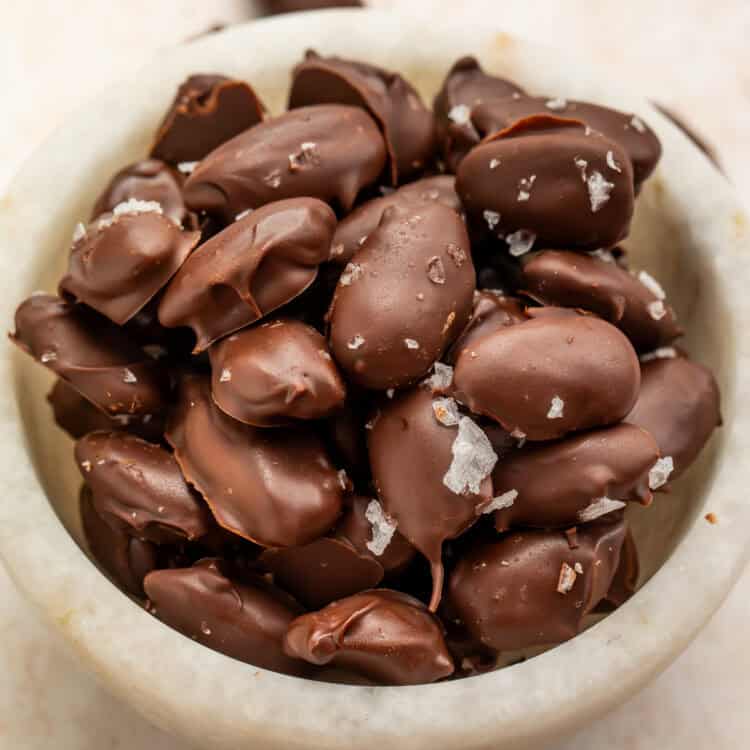 Homemade dark chocolate-covered almonds sprinkled with flaky sea salt in a white bowl.