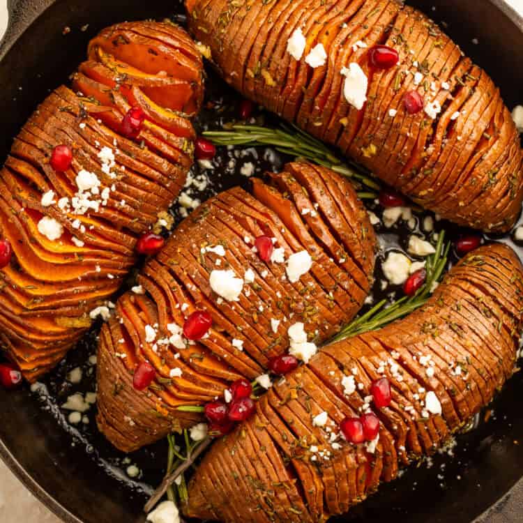 Rosemary maple hasselback sweet potatoes with feta and pomegranate in a cast iron skillet.