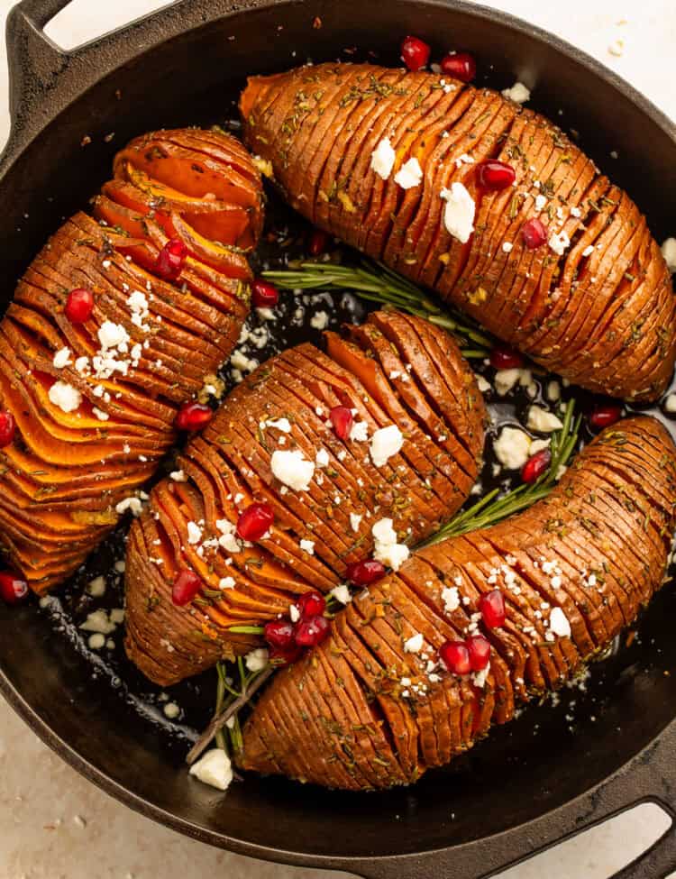 Rosemary maple hasselback sweet potatoes with feta and pomegranate in a cast iron skillet.
