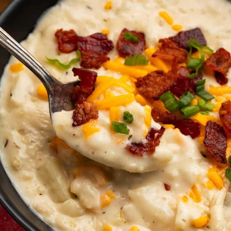 Spoonful of creamy copycat Outback potato soup with potato chunks, bacon, Colby Jack cheese, and green onions.