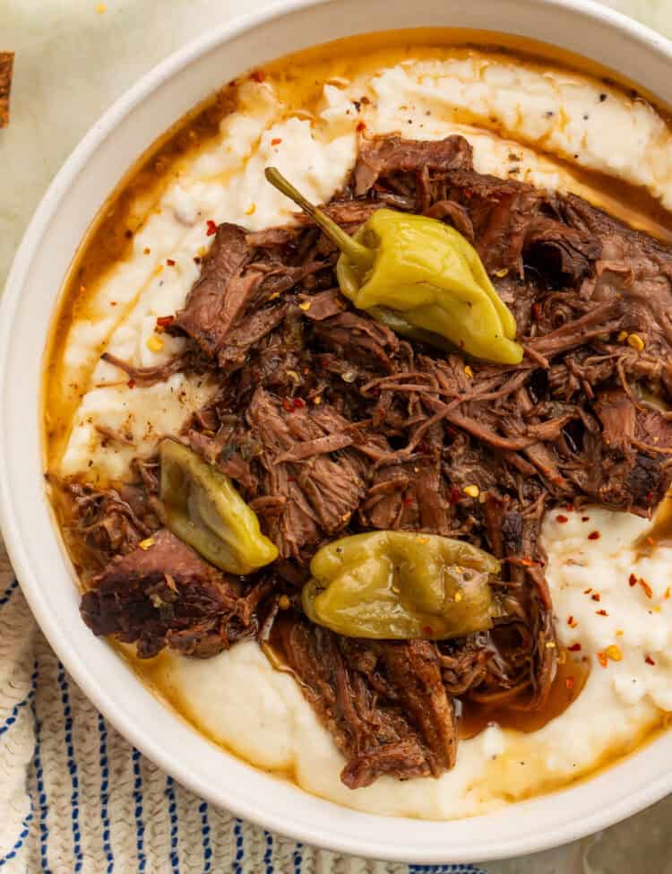 Bowl of shredded Paleo Mississippi Pot Roast with whole pepperoncini and savory juices over mashed potatoes.