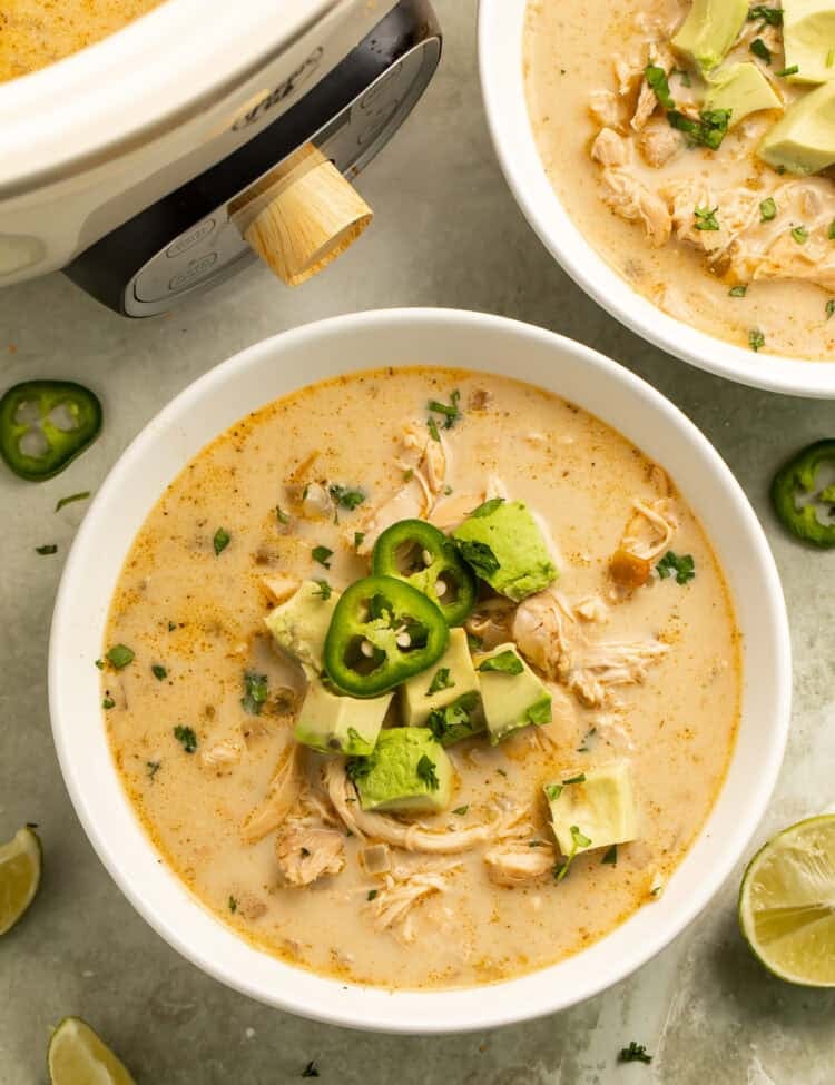 Wooden spoon scooping shredded chicken and green chiles from creamy paleo white chicken chili in a slow cooker.