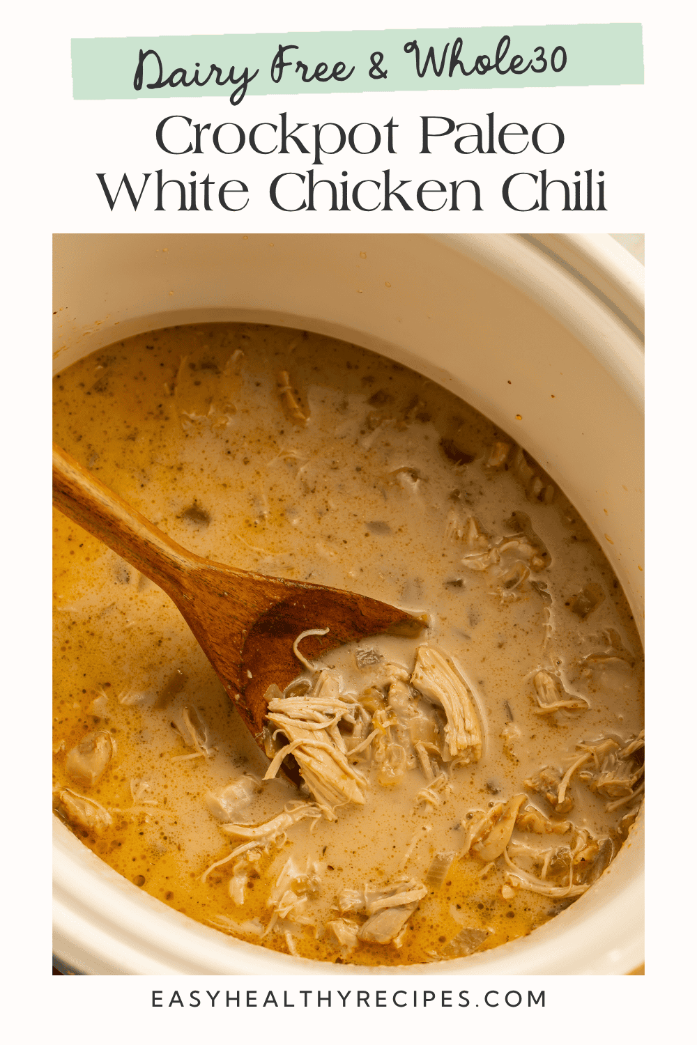 Creamy crockpot paleo white chicken chili with shredded chicken and green chiles on a wooden spoon in the slow cooker.