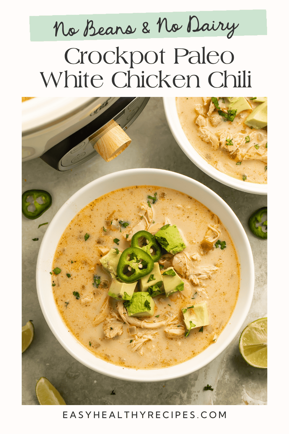 Crockpot paleo white chicken chili topped with avocado, fresh jalapeño, and cilantro in a white bowl, with lime wedges alongside.