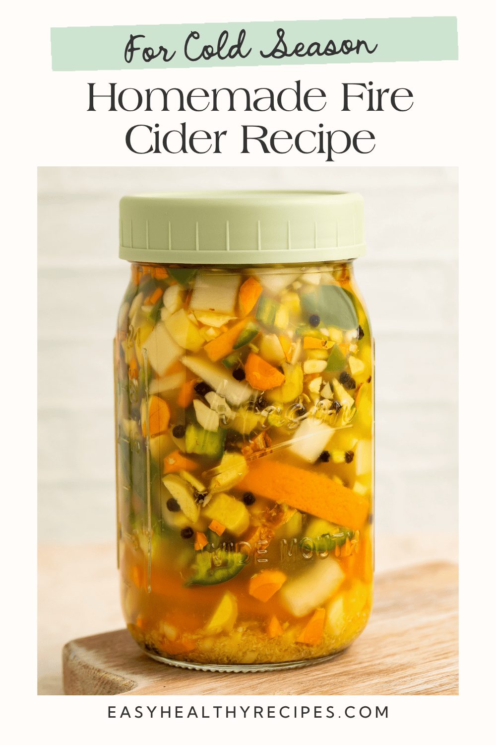 Homemade fire cider recipe showing ginger, turmeric, garlic, citrus, and peppers infusing in a jar