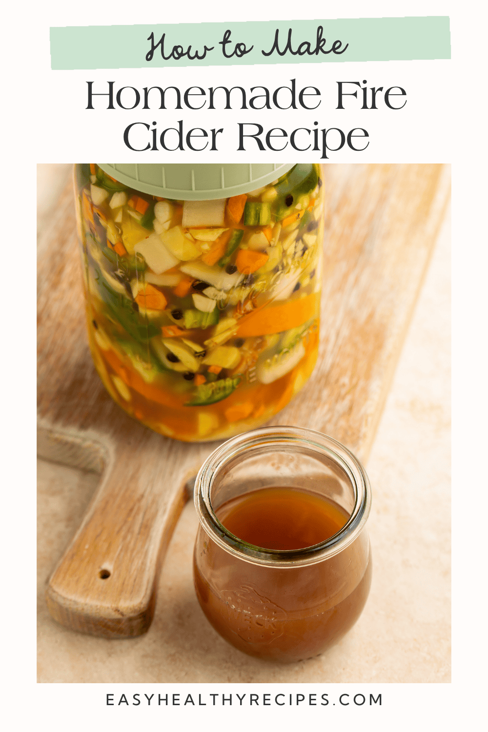 Homemade fire cider in a glass beside a jar of ingredients with text reading “How to Make”
