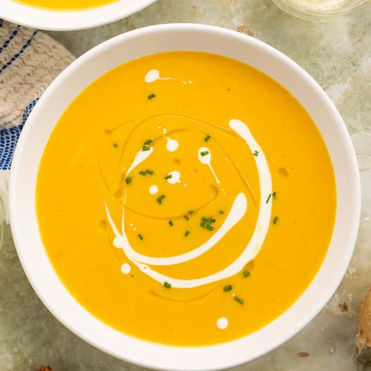 Overhead view of Instant Pot butternut squash soup in a white bowl with a creamy swirl, chives, and bread alongside.