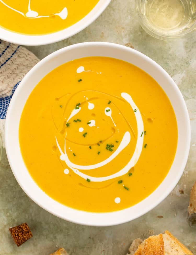 Overhead view of Instant Pot butternut squash soup in a white bowl with a creamy swirl, chives, and bread alongside.