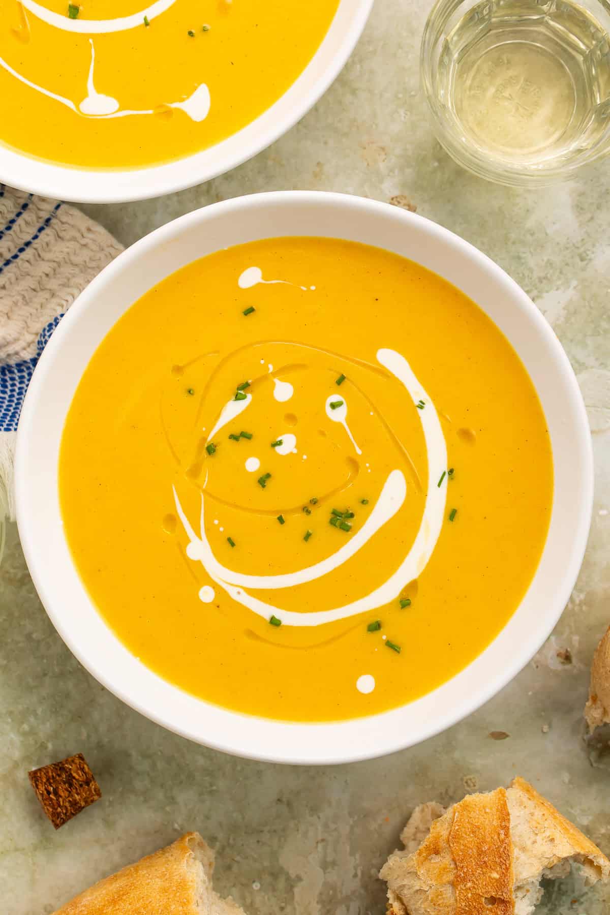 Overhead view of Instant Pot butternut squash soup in a white bowl with a creamy swirl, chives, and bread alongside.