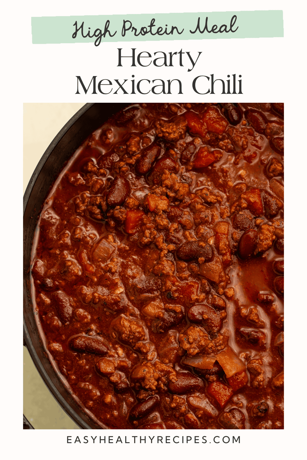 Close-up of thick Mexican chili with ground meat, kidney beans, tomatoes, and chopped onions in a black pot.
