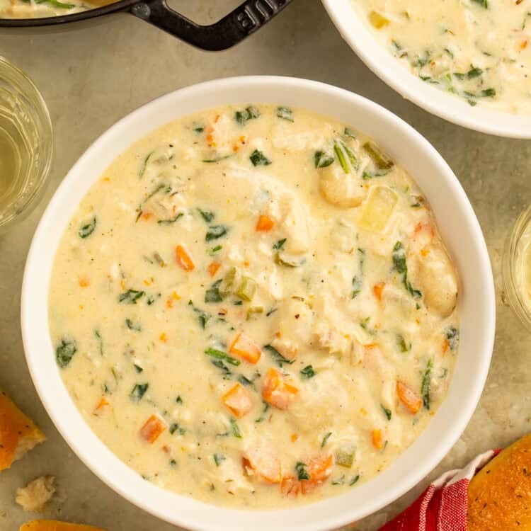Overhead view of copycat Olive Garden chicken gnocchi soup in a white bowl with golden breadsticks alongside.