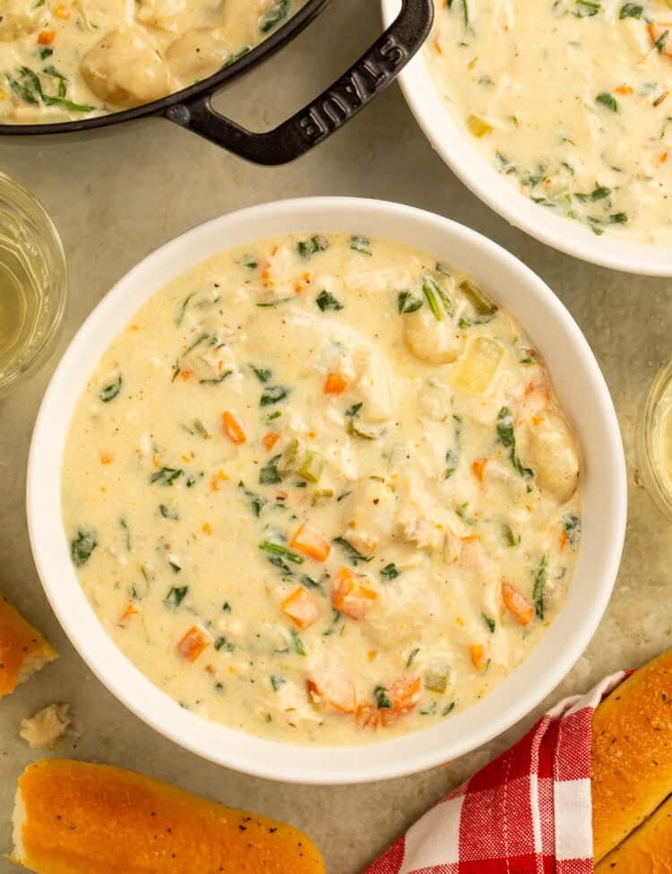 Overhead view of copycat Olive Garden chicken gnocchi soup in a white bowl with golden breadsticks alongside.