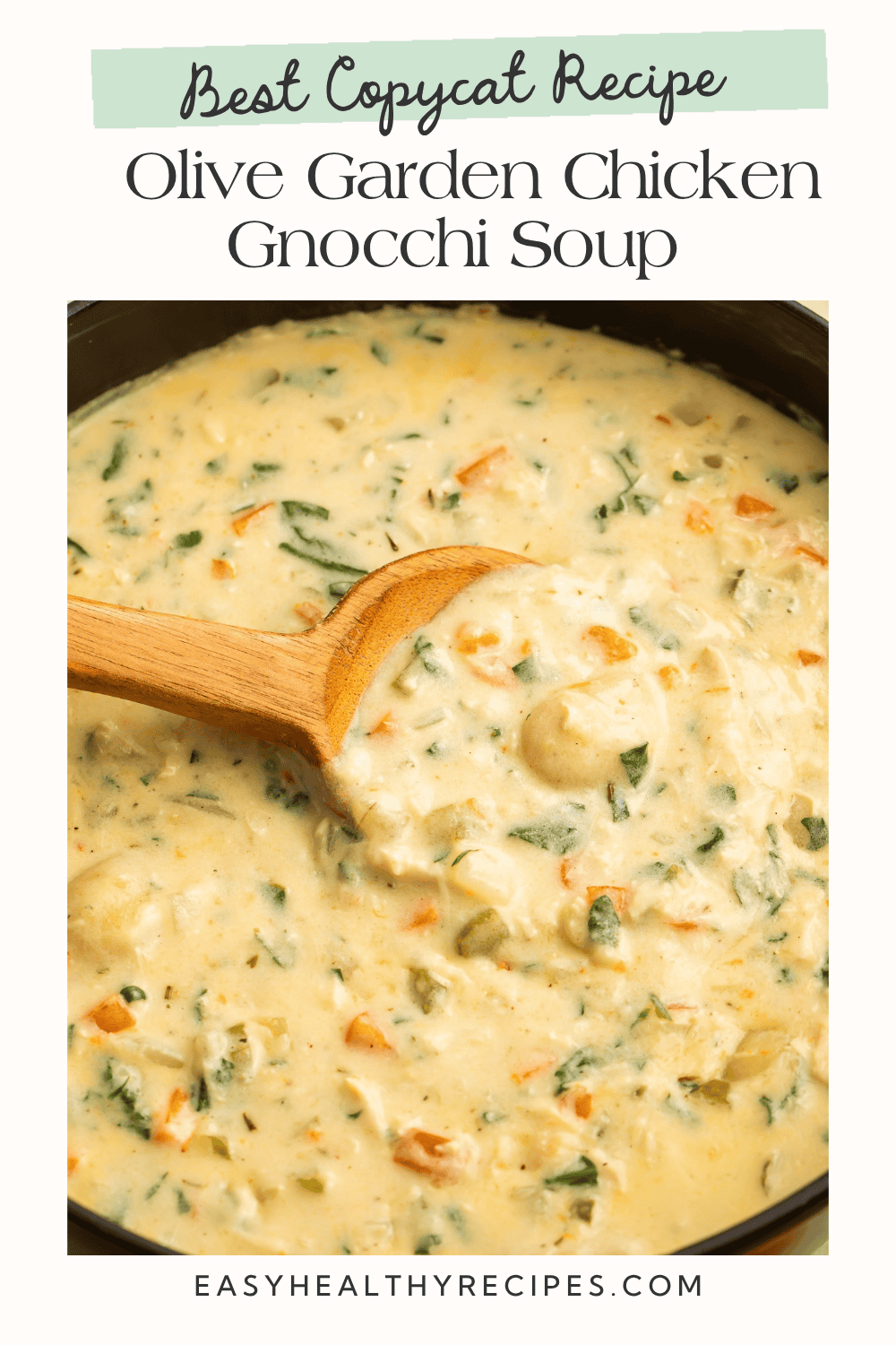 Creamy chicken gnocchi soup with spinach and vegetables in a pot with a wooden spoon.