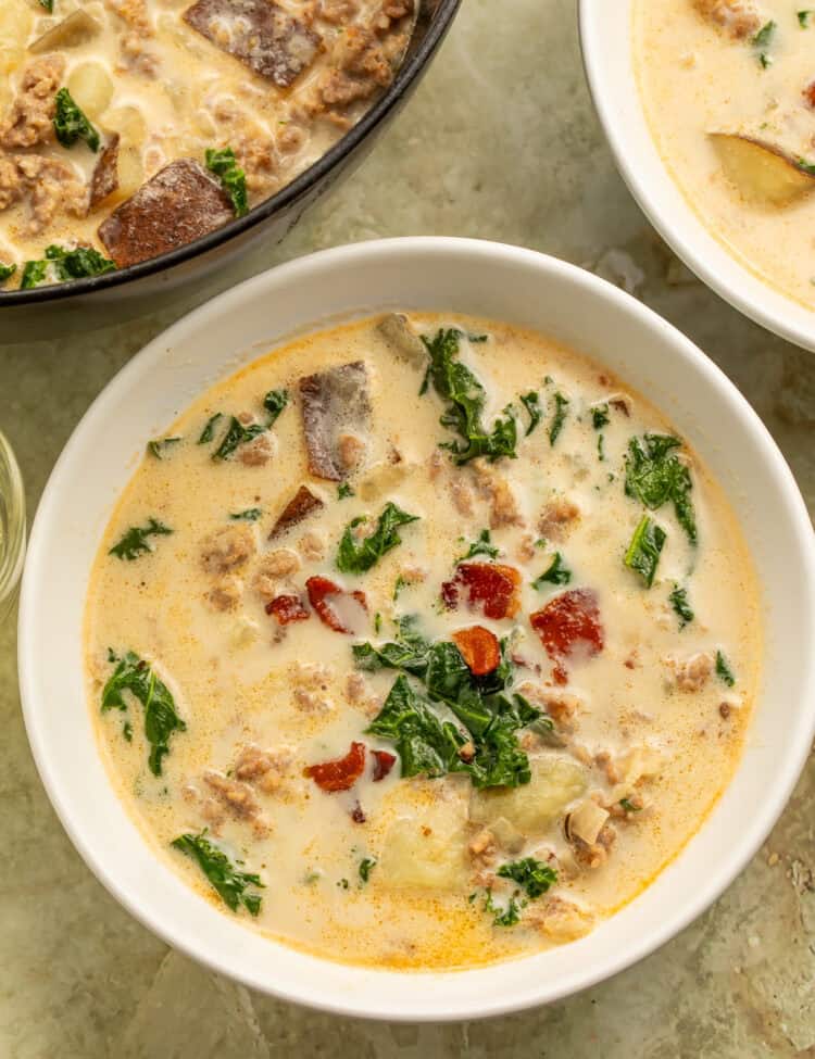 Olive Garden copycat zuppa toscana in a black Dutch oven with creamy broth, sausage, sliced potatoes, kale, and bacon.