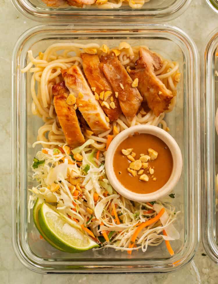 Thai peanut chicken meal prep bowl with rice noodles, cabbage slaw, peanut sauce, peanuts, and lime.