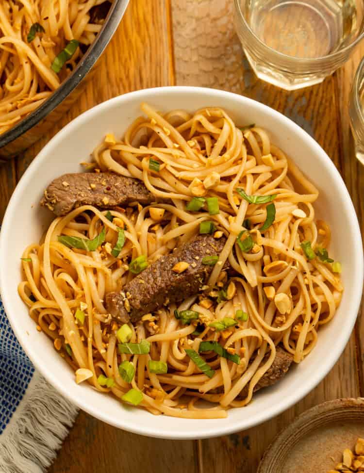 Beef pad Thai in a white bowl with rice noodles, sliced beef, chopped peanuts, and green onions.