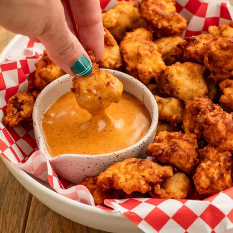 Hand dipping a golden chicken nugget into creamy homemade Chick-fil-A sauce, with more crispy nuggets on the platter.