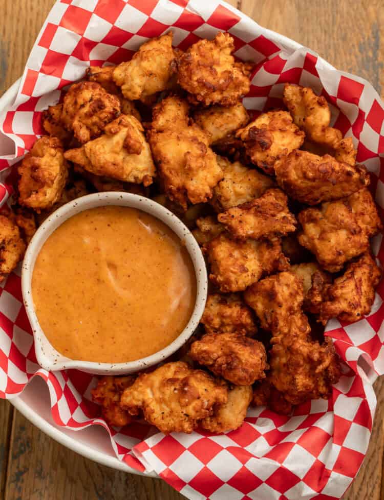 Overhead view of homemade Chick-fil-A sauce in a small bowl surrounded by golden copycat chicken nuggets on red-and-white paper.