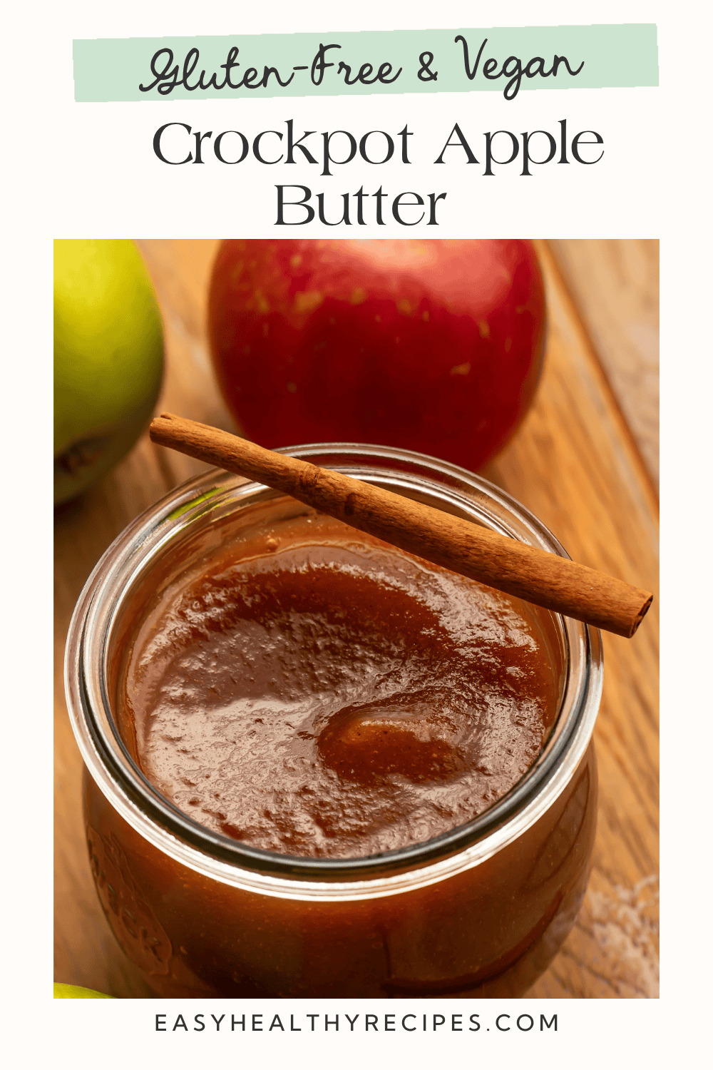 Smooth crockpot apple butter in a glass jar with a cinnamon stick and fresh apples, a gluten-free and vegan fall spread.