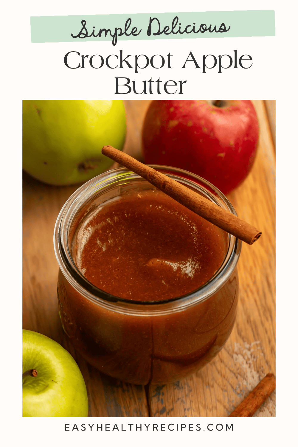 Silky slow cooker apple butter in an open jar, with a cinnamon stick across the rim and sweet-tart apples alongside.