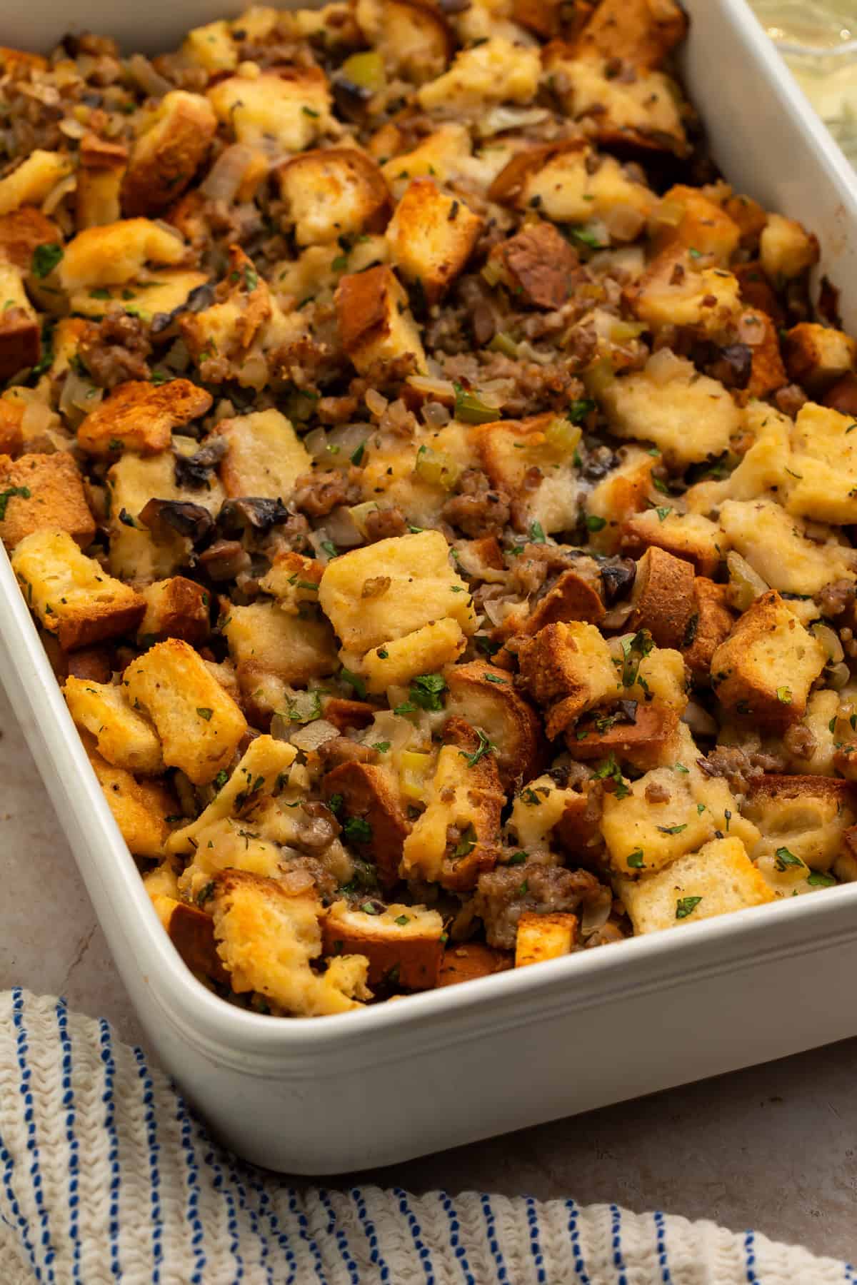 Gluten free stuffing with golden toasted bread cubes, sausage, mushrooms, celery, and herbs in a white baking dish.