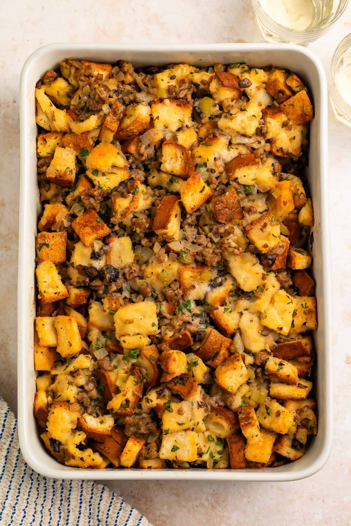 Top view of gluten free stuffing with sausage, golden bread cubes, mushrooms, celery, and chopped herbs in a rectangular dish.