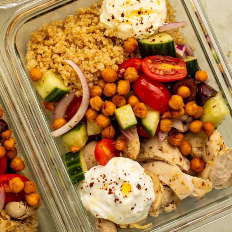 Close-up of a Greek chicken meal prep bowl with farro, roasted chickpeas, cucumber-tomato salad, whipped feta, and tzatziki.