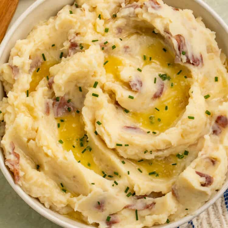Overhead view of red skin mashed potatoes topped with melted butter and chives in a cream-colored serving bowl.