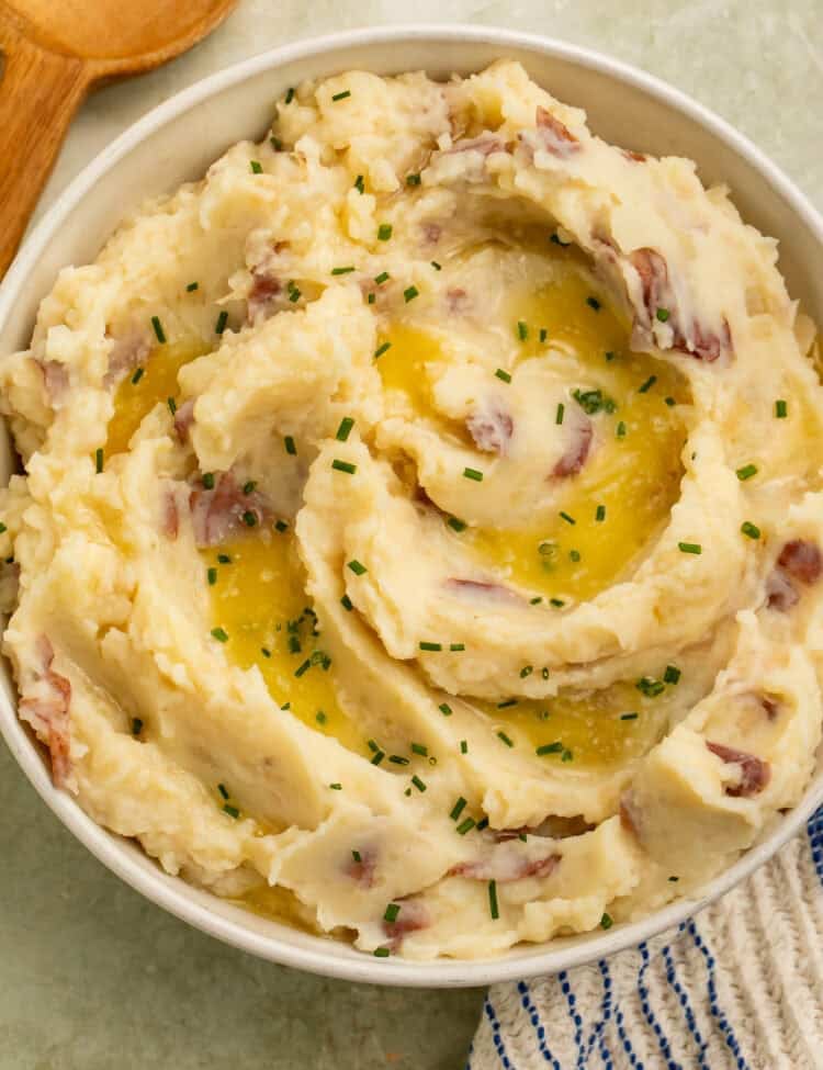 Overhead view of red skin mashed potatoes topped with melted butter and chives in a cream-colored serving bowl.
