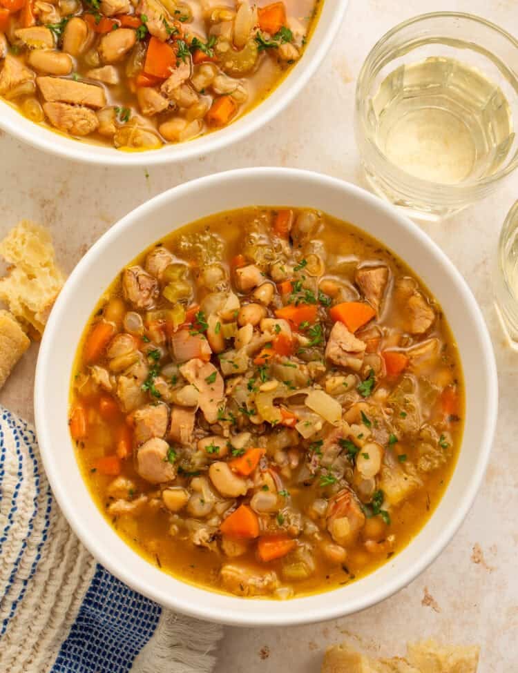Two bowls of smoked turkey soup with white beans, carrots, celery, and onions in golden broth.