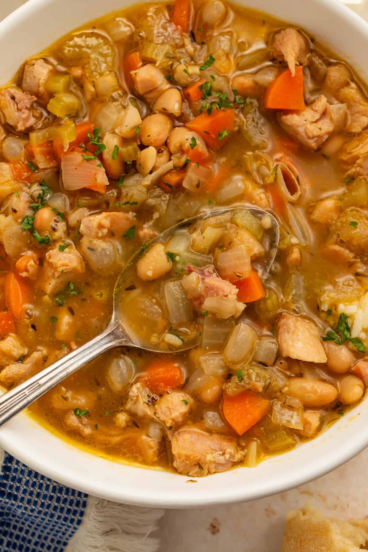 Close up of smoked turkey soup with a spoon holding turkey, white beans, and vegetables in golden broth.